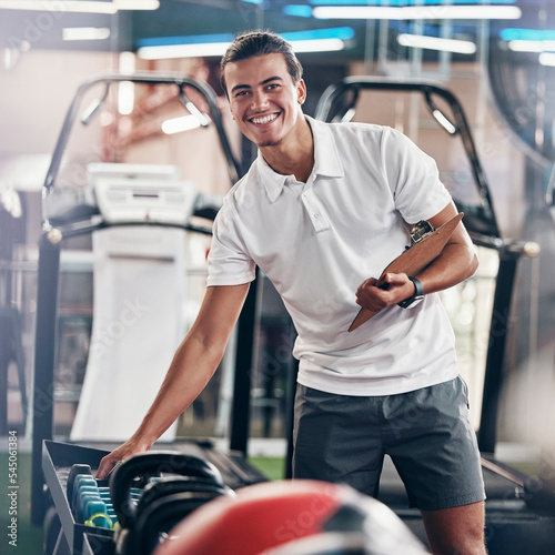 Fototapeta Naklejka Na Ścianę i Meble -  Training, portrait and fitness coach doing inspection of equipment at the gym. Wellness, sport and happy trainer doing check, planning and working at a club for athlete health, sports and workout