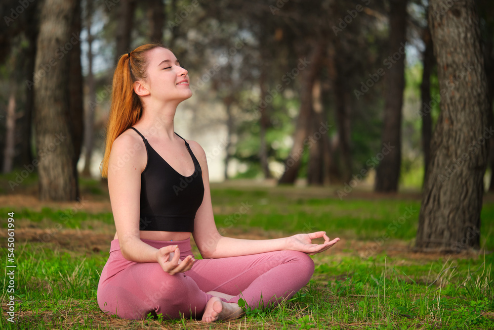 Redhead young woman meditating in a forest. Meditation in nature.