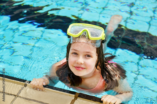 Cute happy young girl in goggles swimming and snorking in the swimming pool. Happy child in summer in outdoor pool. Sports and active children. photo