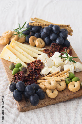 Cheese plate served with grapes, olives, crackers and dried tomatoes on a wooden background, selective focus