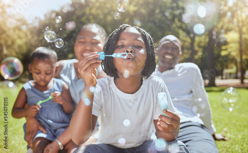 Happy, nature and black family blowing bubbles while playing, bonding and enjoying summer in the park. Happiness, father and mother with children having fun together in a green garden in South Africa