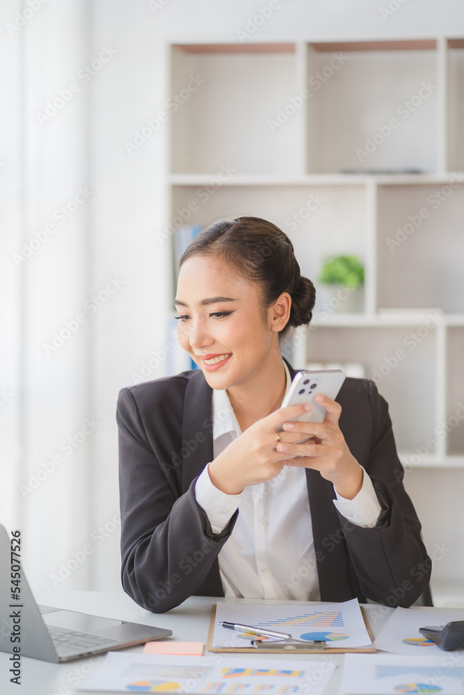 Young beautiful asian woman using smartphone and working with laptop while sitting at office desk, working from home concept. Young beautiful asian woman using smartphone and working with laptop while sitting at office desk, working from home concept.
