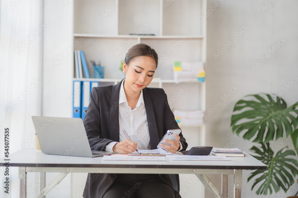 Young beautiful asian woman using smartphone and working with laptop while sitting at office desk, working from home concept. Young beautiful asian woman using smartphone and working with laptop while sitting at office desk, working from home concept.