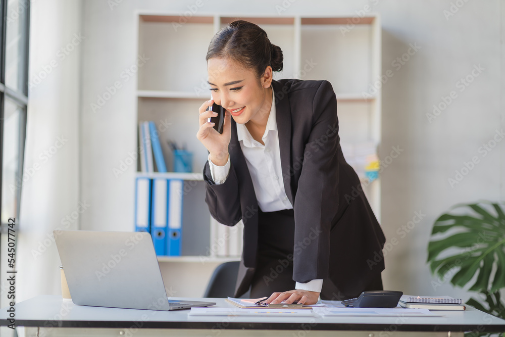Young beautiful asian woman using smartphone and working with laptop while sitting at office desk, working from home concept. Young beautiful asian woman using smartphone and working with laptop while sitting at office desk, working from home concept.