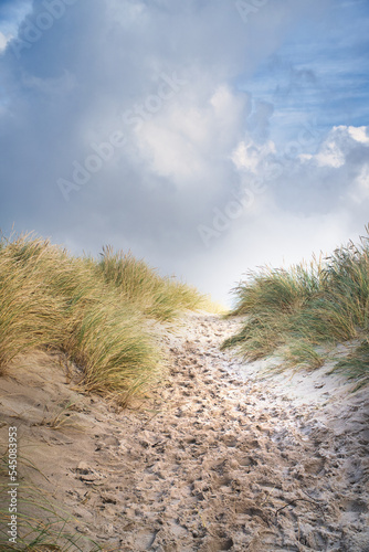 Beach crossing in Denmark by the sea. Dunes, sand water and clouds on the coast