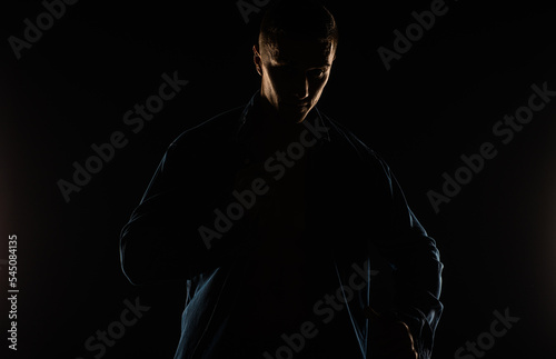 Portrait of a guy putting on his shirt and posing in studio while standing, silhouette