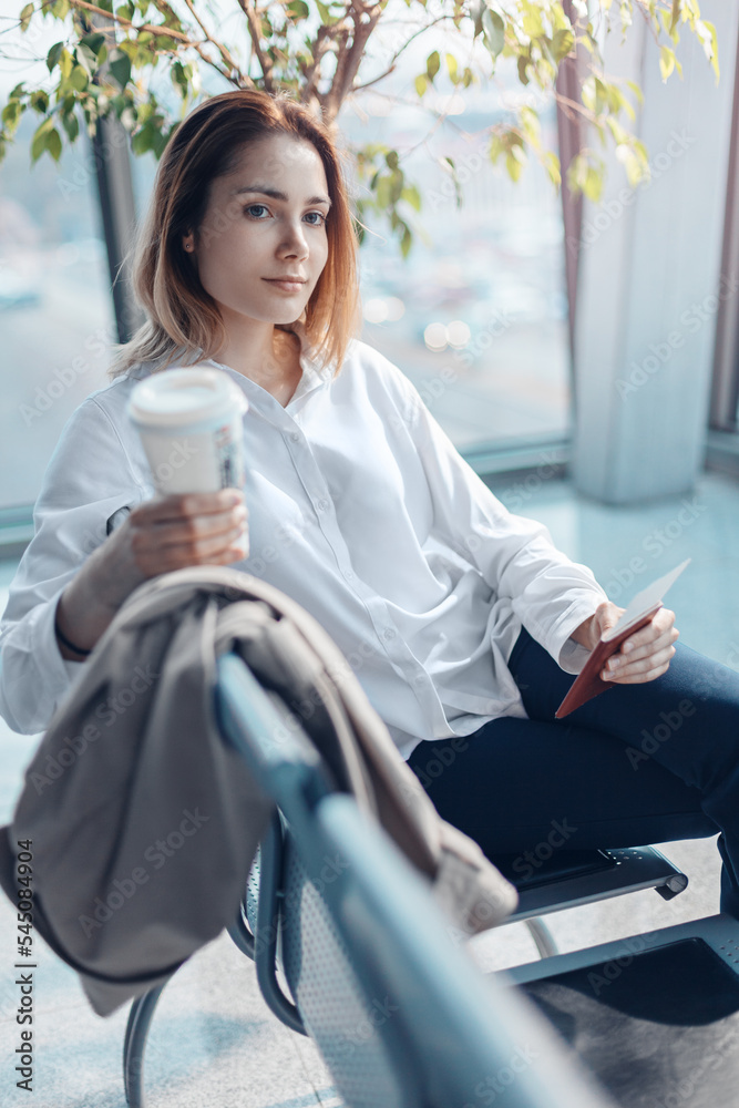 Young woman with a boarding pass and passport waiting for a flight in the departure hall of an airport.