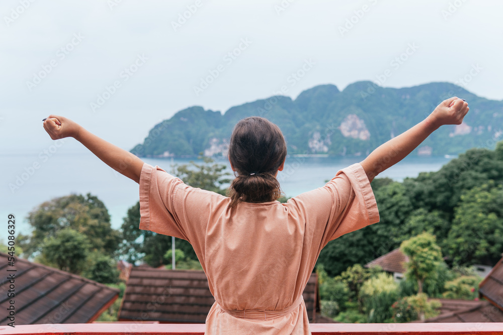 Unrecognizable woman in robe stretching energetically and with her fists clenched while looking at the sea and mountain views in front of her.