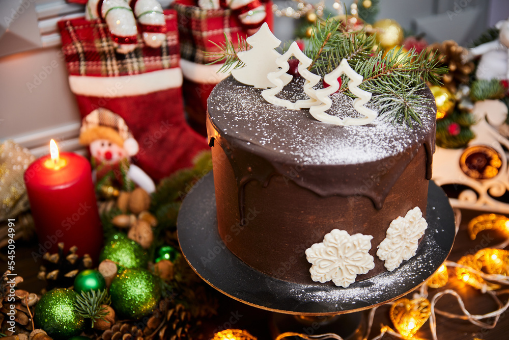 Christmas cake made of chocolate base with chocolate cream, decorated with Christmas trees and white chocolate snowflakes