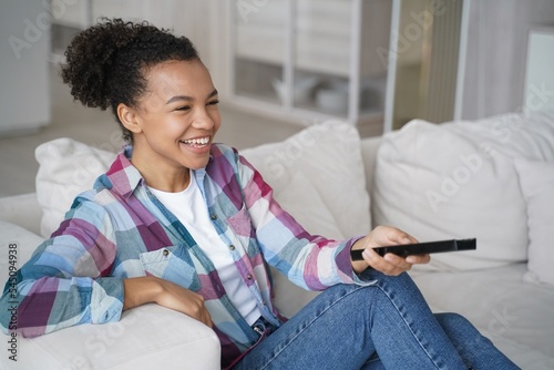 Laughing mixed race girl watching TV, comedy show, movie, television series sitting on couch at home