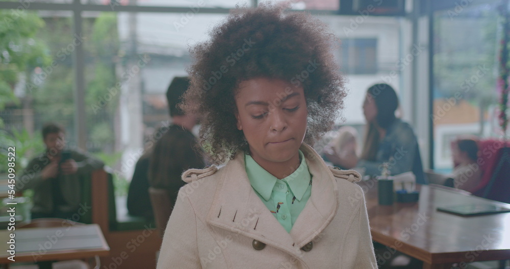One pensive black woman standing in line at coffee shop. A thoughtful African American female customer waits at cafe restaurant biting lip