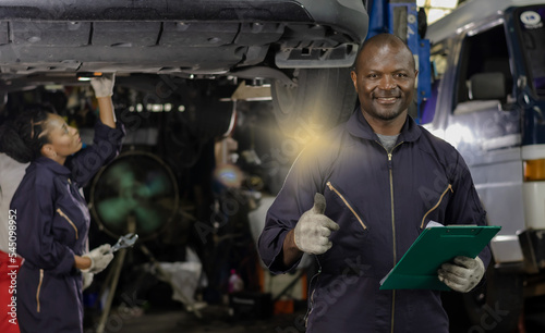 Black mechanic man working in autorepair shop with black mechanic woman background, Car Mechanic Concept photo