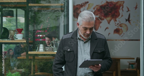 A middle aged entrepreneur owner of coffee shop managing business looking at tablet device. Portrait of an older manager using modern technology