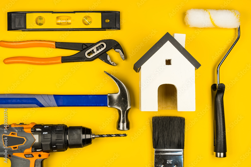 Wooden white house toy and construction tools on yejjow background with copy space.Real estate concept, New house.Home repair concept Wooden white house toy and construction tools on yejjow background with copy space.Real estate concept, New house.Home repair concept