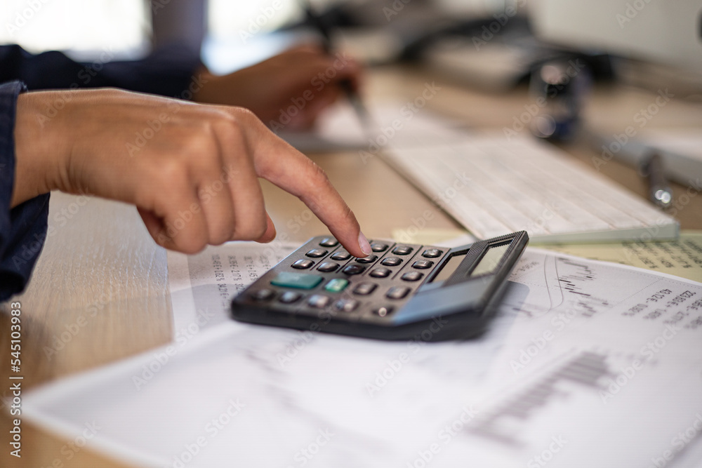 Close up woman hand, typing on a calculator. Desk with keyboard, financial reports, business sheets. Office administrator calculates financial figures. Accounting, ordering and back office services. Close up woman hand, typing on a calculator. Desk with keyboard, financial reports, business sheets. Office administrator calculates financial figures. Accounting, ordering and back office services.