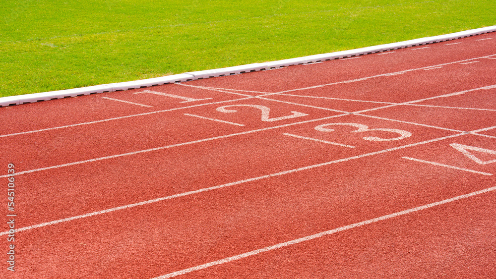 Fototapeta premium Red synthetic running tracks with numbers and green field in athletic outdoors stadium