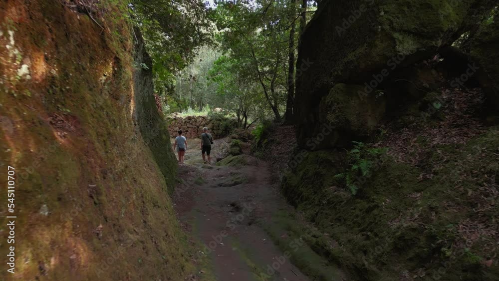 Two persons walking through ancient Etruscan path way at famous Tuscany town Pitigliano, built on tufa rocks with old medieval buildings near scenic Siena and Florence, Italy. 4K drone as aerial view. Two persons walking through ancient Etruscan path way at famous Tuscany town Pitigliano, built on tufa rocks with old medieval buildings near scenic Siena and Florence, Italy. 4K drone as aerial view.