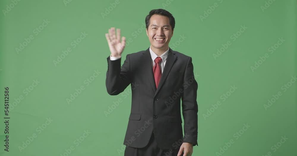 An Asian Business Man Waving Hand And Smiling While Standing On Green Screen In The Studio
An Asian Business Man Waving Hand And Smiling While Standing On Green Screen In The Studio