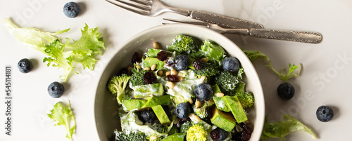 bowl with salad with broccoli, avocado and blueberries on a light table