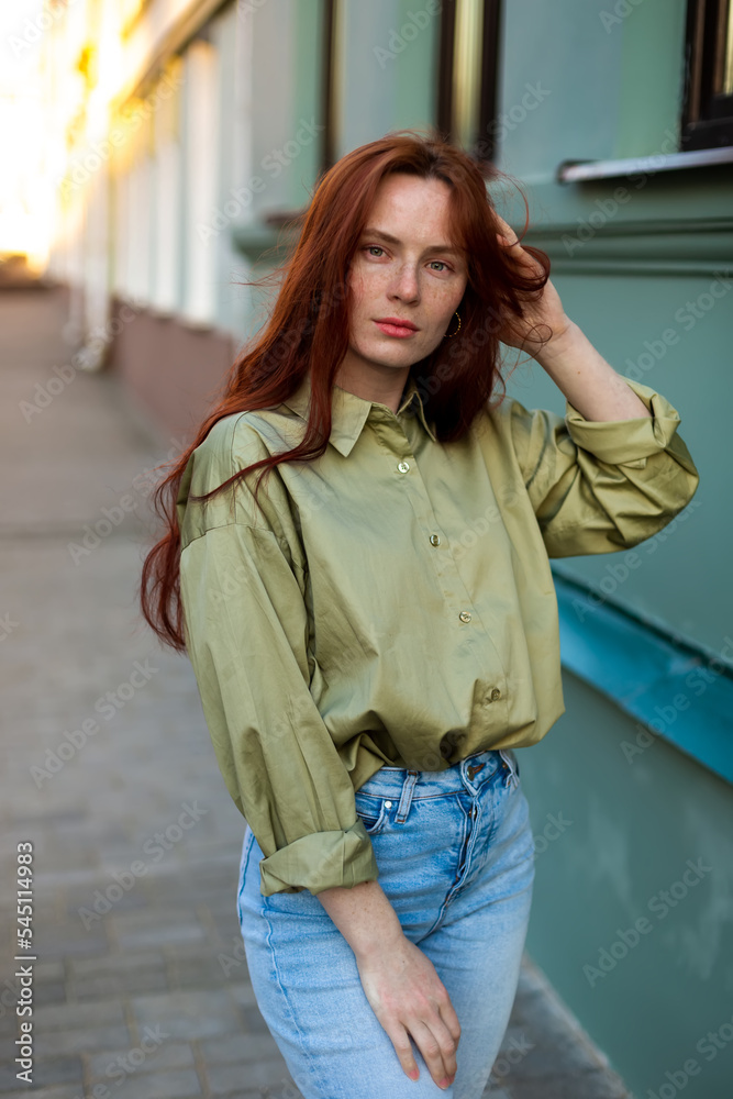 Fototapeta premium Young woman with long ginger hair outdoors in city. Young woman face with freckles