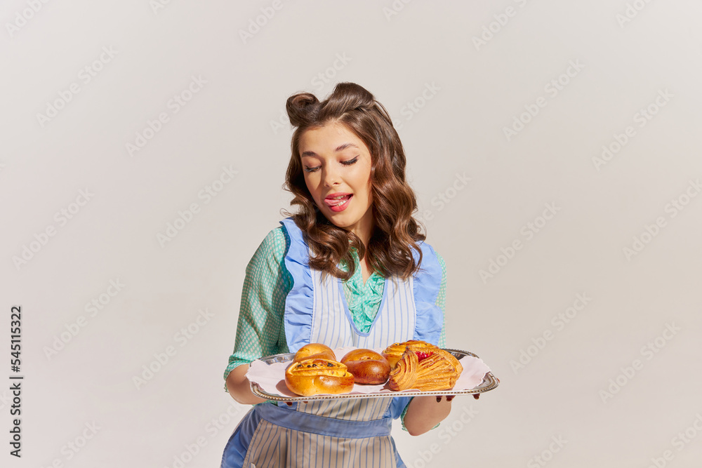 Portrait of stylish young woman, housewife with freshly baked buns isolated over grey background