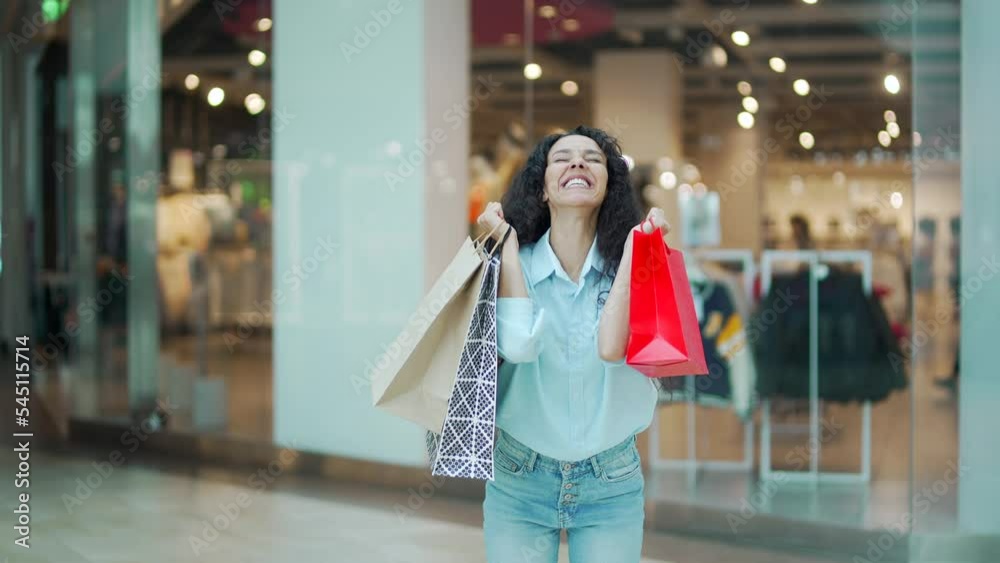 Portrait crazy young shopaholic woman rejoices jump with happiness happy glad shopping mall center after sale discount look at camera joyful smiling with gift bags with purchases satisfied wonder girl