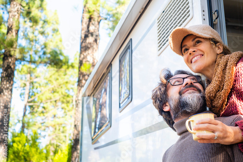 Happy couple enjoying outdoor forest destination smiling together outside their camper van vehicle. Concept of alternative travel vacation and free off grid lifestyle. People traveler with motorhome