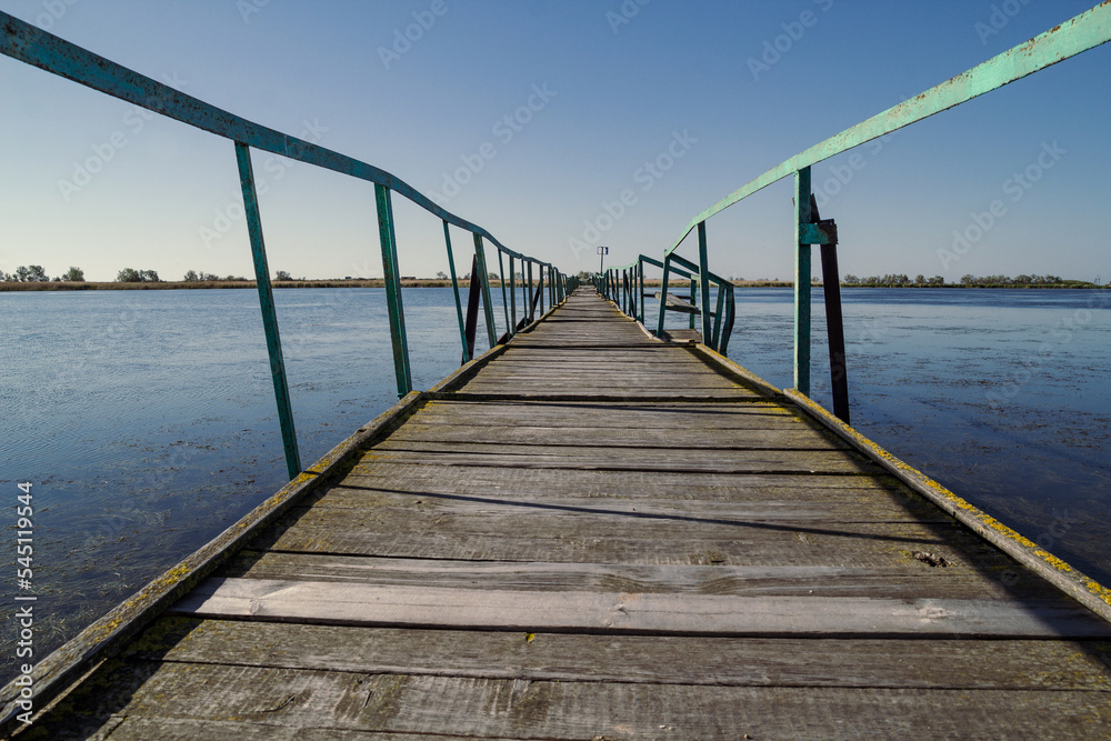 Wooden bridge over river landscape photo. Beautiful nature scenery photography with wide watercourse on background. Idyllic scene. High quality picture for wallpaper, travel blog, magazine, article