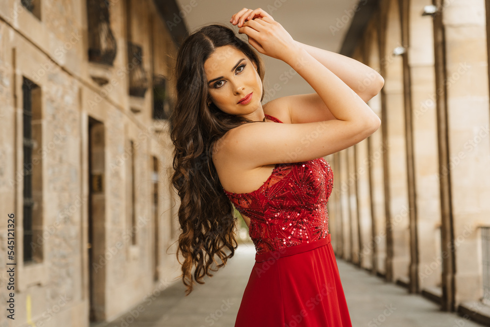 Caucasian woman in a red gala dress, portrait of the model next to some columns