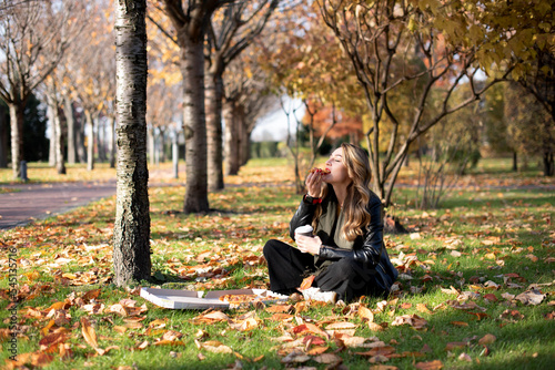 Young girl eats pizza in the park enjoying autumn nature..