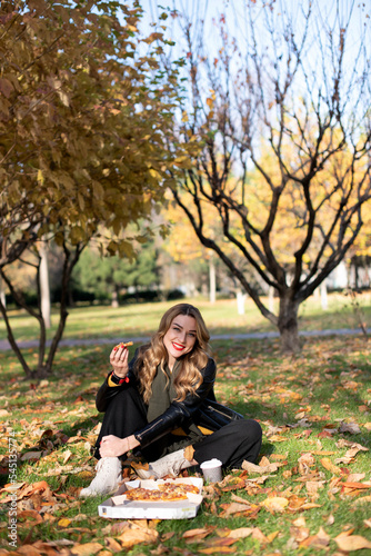 Young girl eats pizza in the park enjoying autumn nature..