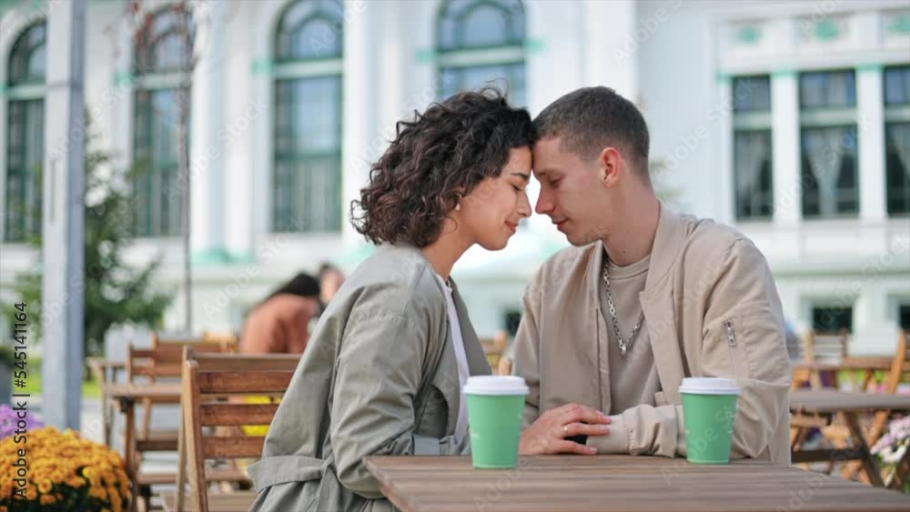 A romantic couple outdoors near a cafe. Holding hands, smiling with closed eyes, coffee on the table. Autumn atmosphere. Slow motion A romantic couple outdoors near a cafe. Holding hands, smiling with closed eyes, coffee on the table. Autumn atmosphere. Slow motion