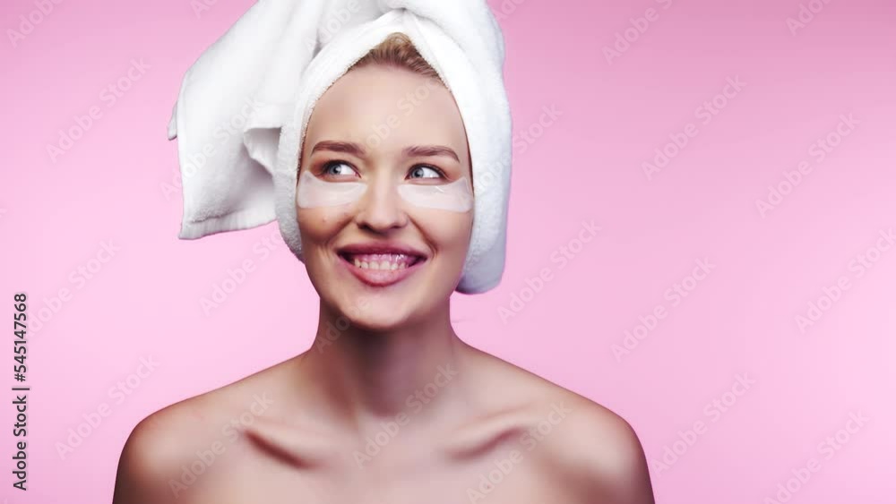 Beautiful caucasian woman applying moisturizer cream on her smiling face. Smiling woman with perfect makeup on pink background with a towel on his head. Beauty concept Beautiful caucasian woman applying moisturizer cream on her smiling face. Smiling woman with perfect makeup on pink background with a towel on his head. Beauty concept
