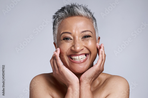 Beauty, skincare and portrait of senior woman in studio on gray background. Makeup cosmetics, smile and happy mature female model from India touching face for facial or healthy skin treatment routine