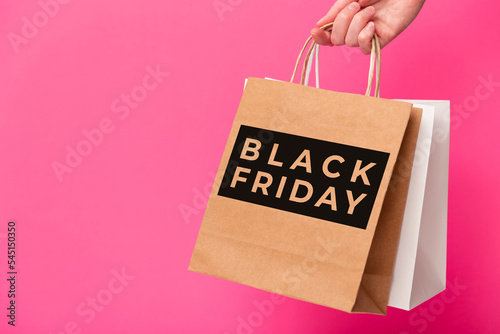 Black Friday, female hand holding two shopping bags isolated on pink background. Black friday sale, discount, shopping and ecology concept.