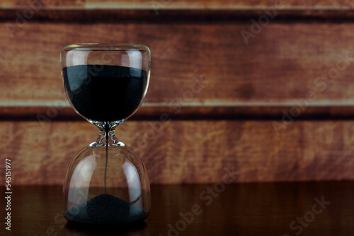 Black Sand Hourglass on a Polished Wooden Shelf