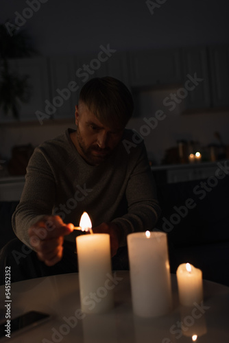 Obraz na plátně man sitting in dark kitchen during power outage and lighting candles