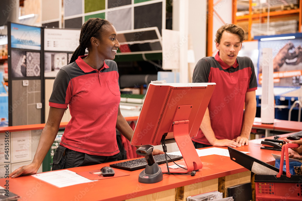 Smiling female cashier with male colleague standing at checkout in hardware store