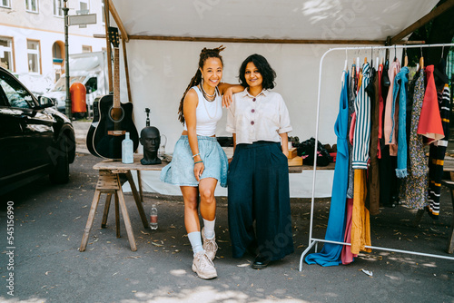 Female partners standing against table by merchandise in stall at flea market