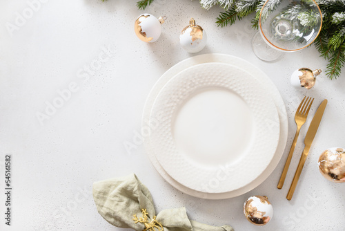 Beautiful Christmas festive table setting with white plate, golden balls and napkin ring as deer on white background. View from above. Copy space. Xmas festive dinner.