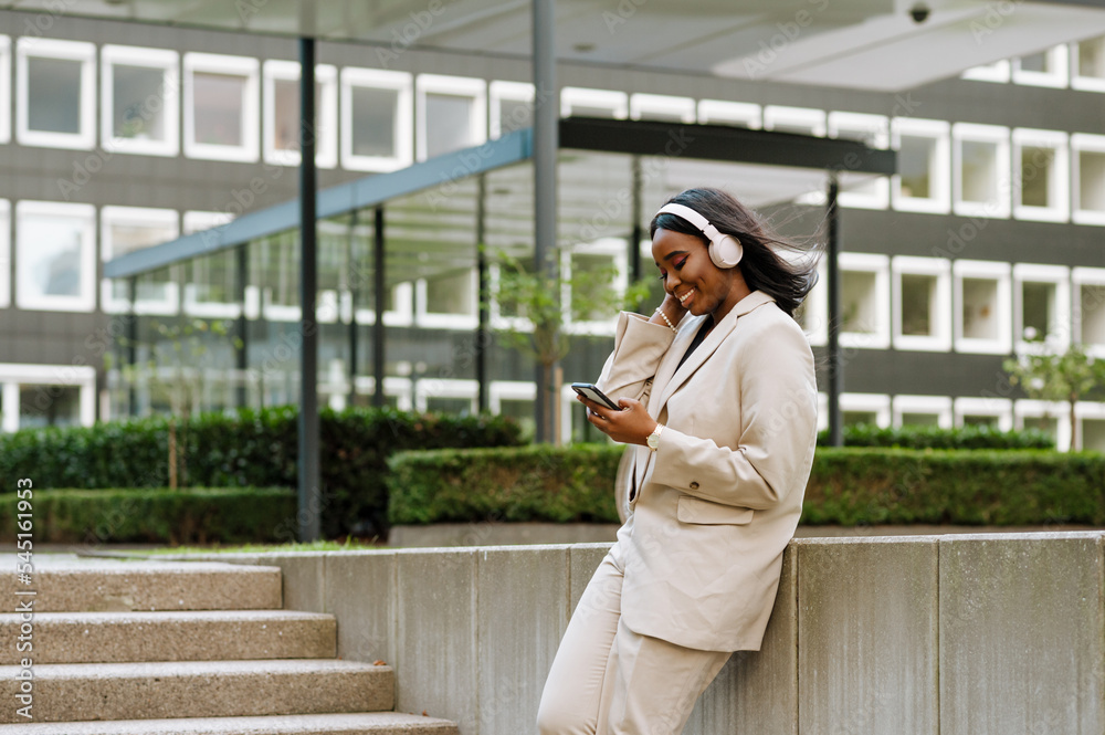Young black businesswoman using cellphone and headphones outdoors
