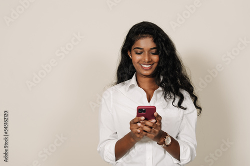 Young brunette indian woman smiling and using cellphone