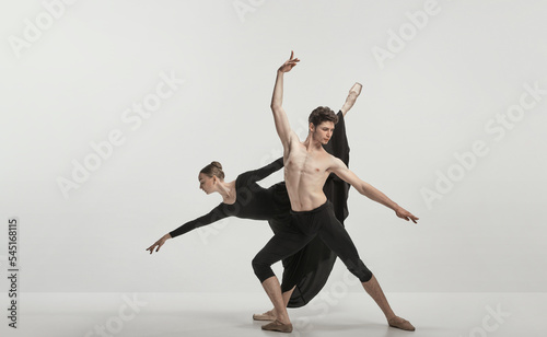 Young man and woman, ballet dancers performing isolated over grey studio background. Flexibility and tenderness