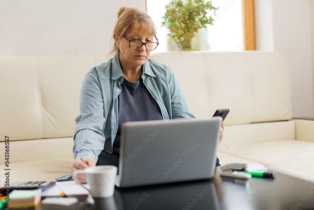 Elderly businesswoman working from home office, talking on mobile phone call, laughing, enjoying telephone conversation, using online app on laptop for consulting client Elderly businesswoman working from home office, talking on mobile phone call, laughing, enjoying telephone conversation, using online app on laptop for consulting client