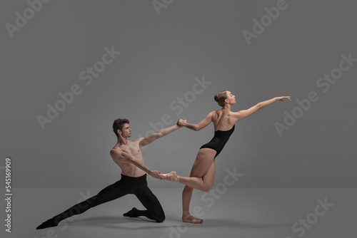 Young man and woman, ballet dancers performing isolated over dark grey studio background. Puzzled position photo