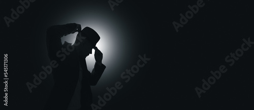 The man puts a hat on his head. Light source in the background