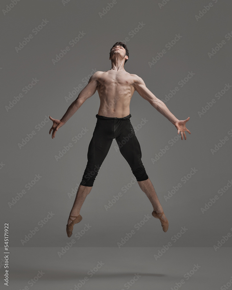 Portrait of young muscular man, ballet dancer performing isolated over dark grey studio background. Metamorphosis