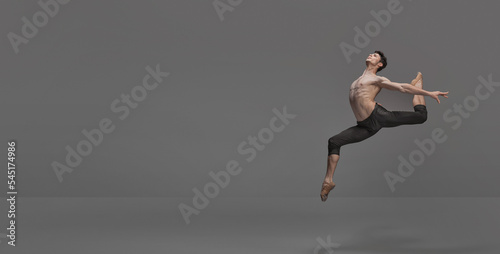 Portrait of young muscular man, ballet dancer performing on stage isolated over dark grey studio background. Flyer © master1305