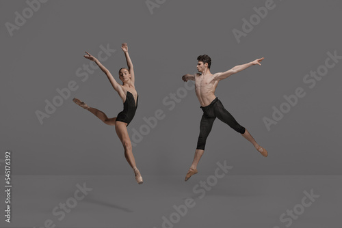 Young man and woman, ballet dancers performing isolated over dark grey studio background. Expressing talent