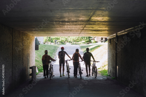 Male and female friends wheeling with cycles while walking through underpass